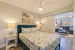 Een slaapkamer met een bed, nachtkastjes, een plafondventilator, een schilderij, een kledingkast en uitzicht op het exterieur.