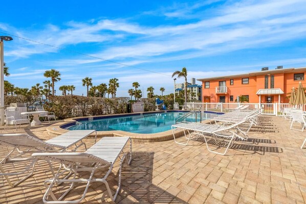 A swimming pool with lounge chairs, palm trees, and a building with a sign.