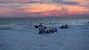 Una spiaggia con persone sedute su sedie a sdraio sotto un cielo al tramonto.