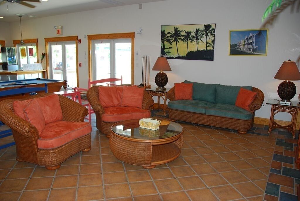 A living room with wicker furniture, a pool table, and a painting of palm trees.