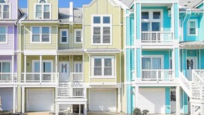 Una hilera de casas coloridas frente a la playa, con barandillas blancas y varios portones de garaje.