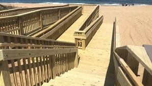 Un paseo marítimo de madera que lleva a una playa arenosa, con el océano al fondo.