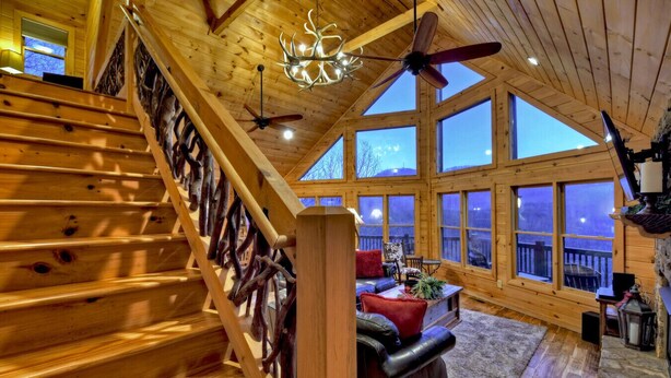 A wooden cabin interior with a staircase, large windows, and a ceiling fan. - Mountain Dream Hideaway | Stylish Cabin w/ Mountain Views, Hot Tub & Game Room (Blue Ridge)