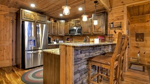 A wooden cabin kitchen with a stone island, stainless steel appliances, and hanging pendant lights. - Mountain Dream Hideaway | Stylish Cabin w/ Mountain Views, Hot Tub & Game Room (Blue Ridge)