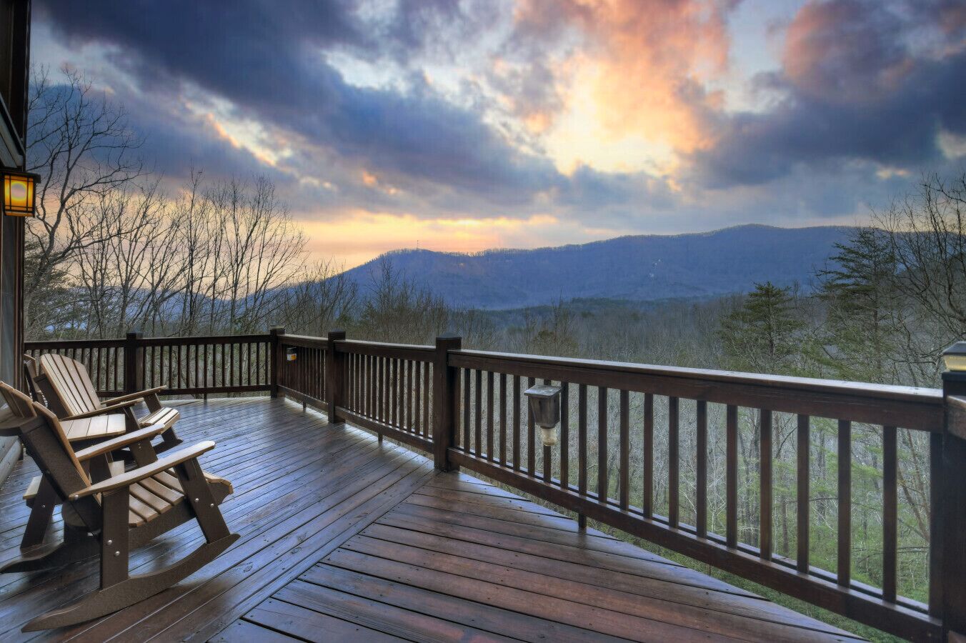 Una terraza de madera con sillas Adirondack y barandilla, con vistas a un paisaje montañoso.