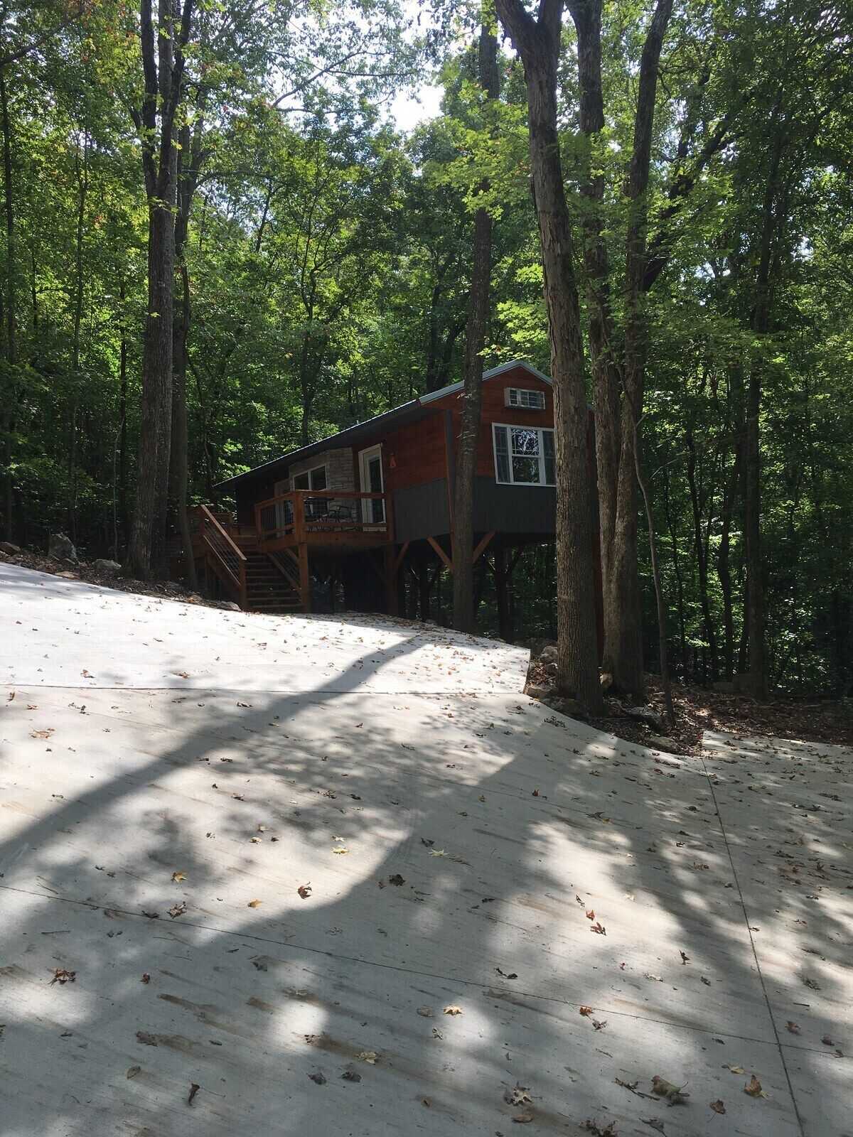 A cabin with a deck, surrounded by trees.