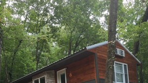 A wooden cabin with a deck, a staircase, and a stone wall.