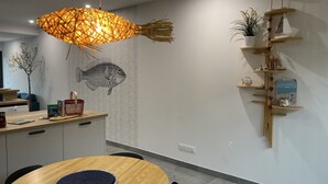 Una zona de menjador moderna amb una taula rodona de fusta, una làmpada penjant de fibra natural i una estanteta amb objectes decoratius.
