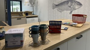 Una cuina amb un taulell, una llauna de cafè, tasses, una cistella vermella i un llibre de cuina.