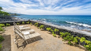 A beachside seating area with lounge chairs and a stone wall.
