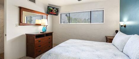 A bedroom with a bed, dresser, mirror, ceiling fan, window, and wall-mounted lamp.