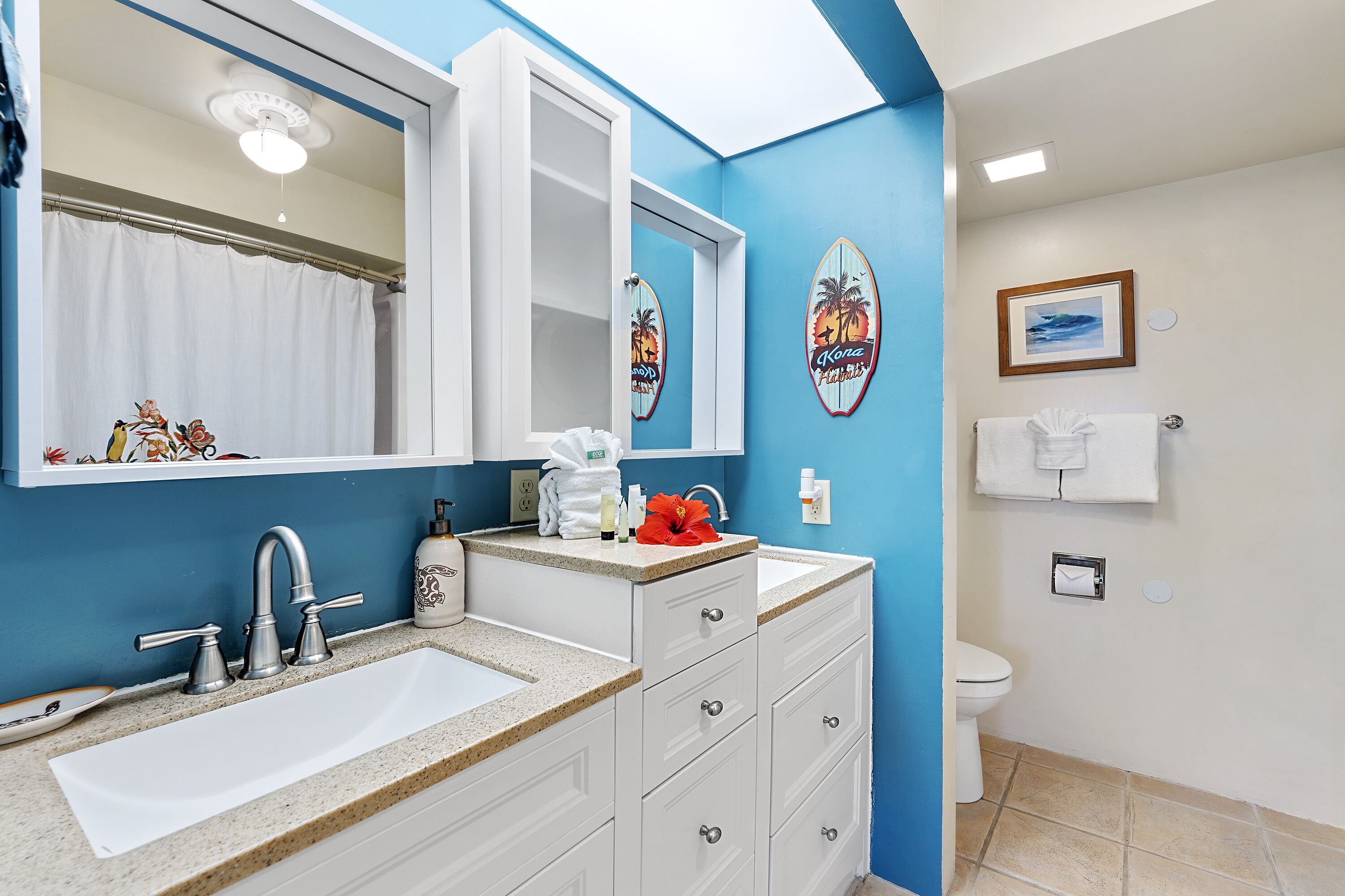 A bathroom with a white sink, a mirror, and a toilet. There are decorative surfboards on the wall.