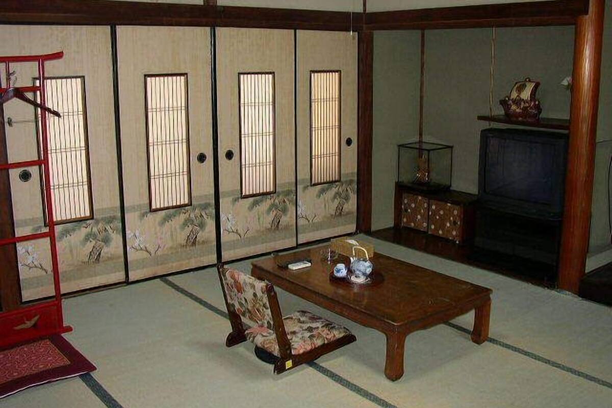 A traditional Japanese room with sliding doors, a television, a wooden table, and a chair.