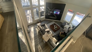 A modern living room with a large window, a ceiling fan, and a flat-screen TV.