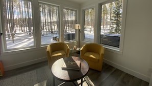 A room with large windows, two yellow armchairs, a small table with a book, and a lamp.