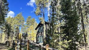 A lodge surrounded by tall pine trees with a wooden fence in the foreground.