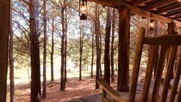 A wooden deck with a bench, surrounded by trees, and a hanging lantern.