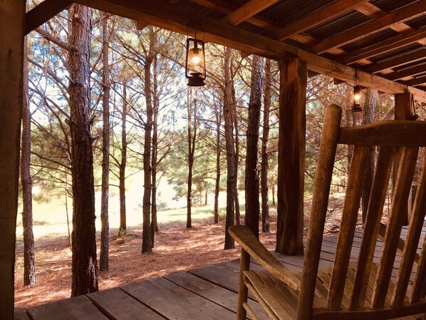 Une terrasse en bois avec un banc, entourée de grands arbres et d’une structure en bois ornée de lanternes suspendues.