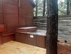 A wooden deck with a hot tub and a metal structure, surrounded by trees.