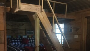 A wooden staircase leading to a lofted sleeping area with a checkered bedspread.