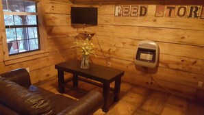 A cozy room with a wooden interior, a black leather couch, a small table with a vase of flowers, a heater, and a TV mounted on the wall.