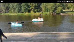 A wooden dock extending into a calm lake with two people on paddle boats.