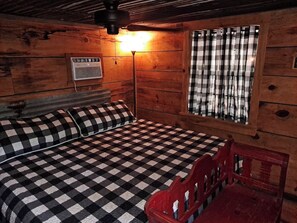 A room with a checkered bedspread, a red chair, a wall-mounted heater, and a window with checkered curtains.