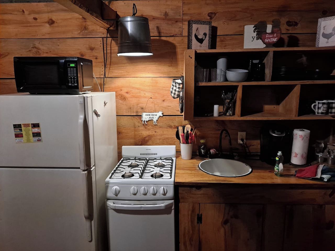 A kitchen with a stove, microwave, refrigerator, wooden shelves, and various kitchen utensils.