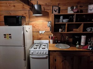 A kitchen with a stove, microwave, refrigerator, wooden shelves, and various kitchen utensils.