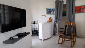 Een woonkamer met een flatscreen televisie aan de muur, een witte kast, een houten schommelstoel en een kleine tafel met een vaas.