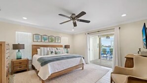 Ein Schlafzimmer mit Bett, Deckenventilator, Nachttisch, Kommode und Blick ins Freie.
