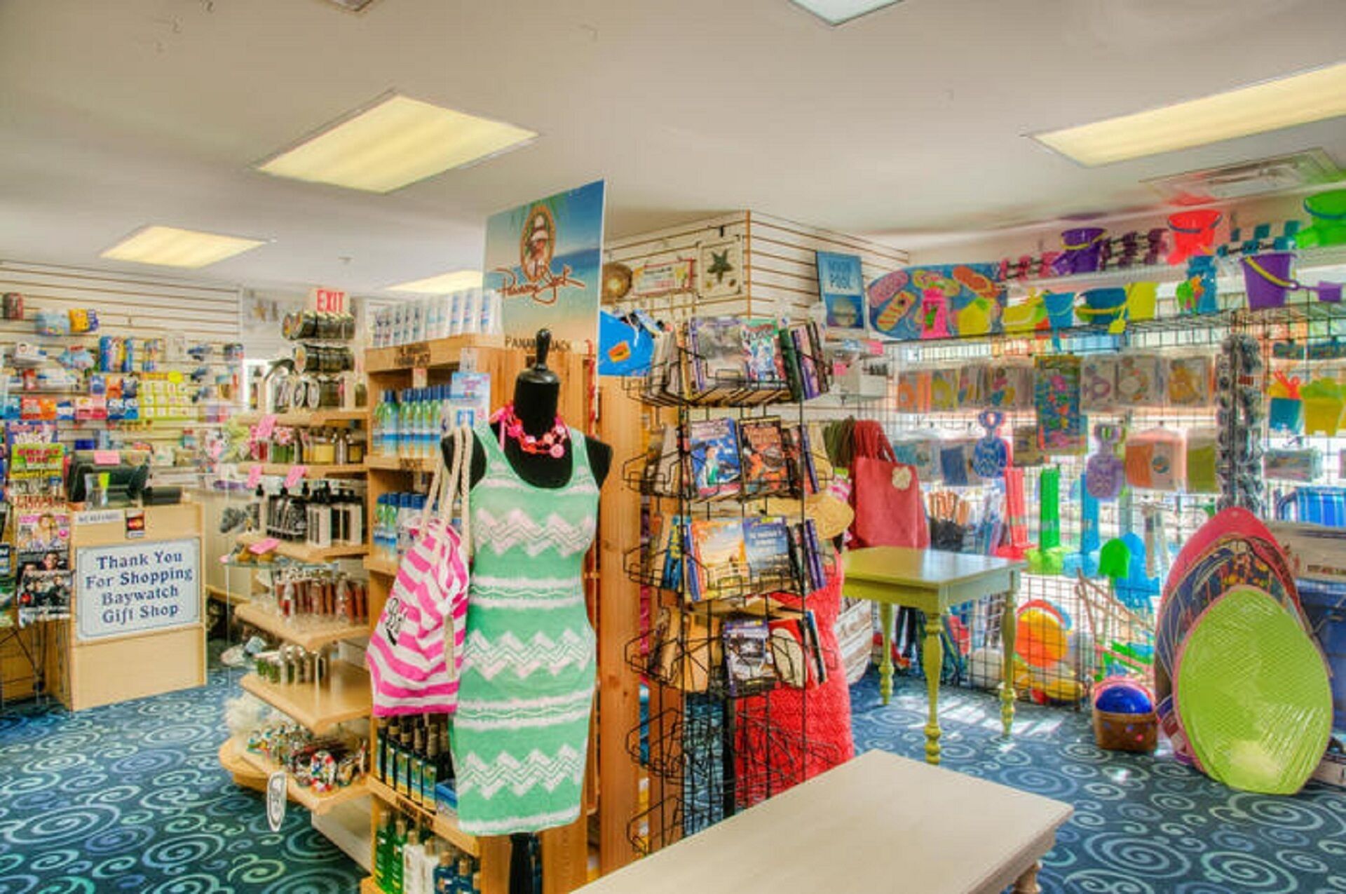 Une boutique de souvenirs proposant divers articles, notamment des livres, des jouets et des sacs, présentés sur des étagères et des présentoirs.
