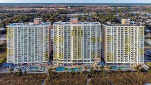 A high-rise hotel with multiple balconies, a pool area, and a beach view.