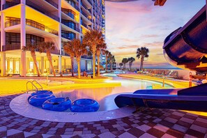 A hotel pool area with a circular water feature, lounge chairs, and palm trees. - Lazy River | Beachfront | Sleeps 10 | Ocean Views (Orange Beach)