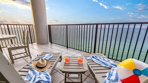 Un balcón con vista al mar, una mesa con bebidas, una pelota de playa y un sombrero de paja.