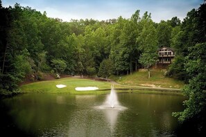 A golf course with a pond, a fountain, and a house in the background. - Apple Valley 63 at Rumbling Bald (Lake Lure)
