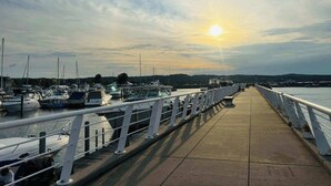 A pier with boats docked, a clear sky, and the sun setting or rising. - Perfect Northern Michigan Escape | Walkable TC Condo | Capri 212 (Traverse City)