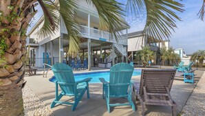 A pool area with Adirondack chairs and a lounge chair, a covered deck, and a building with a balcony. - The Turtle Shell: Home Across from Ocean Crest Pier and Restaurant (Oak Island)
