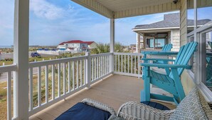 A covered porch with white railings, wicker furniture, and turquoise chairs. - The Turtle Shell: Home Across from Ocean Crest Pier and Restaurant (Oak Island)