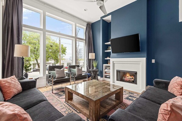 A modern living room with a fireplace, comfortable seating, and a large window offering a view of the outdoors.