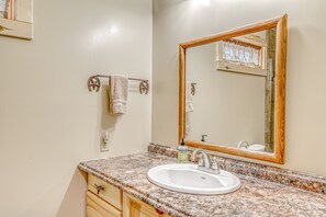 Ein Badezimmer mit einer Granit-Arbeitsplatte, einem weißen Waschbecken, einem spiegel mit Holzrahmen und einem Handtuchhalter mit zwei Handtüchern.