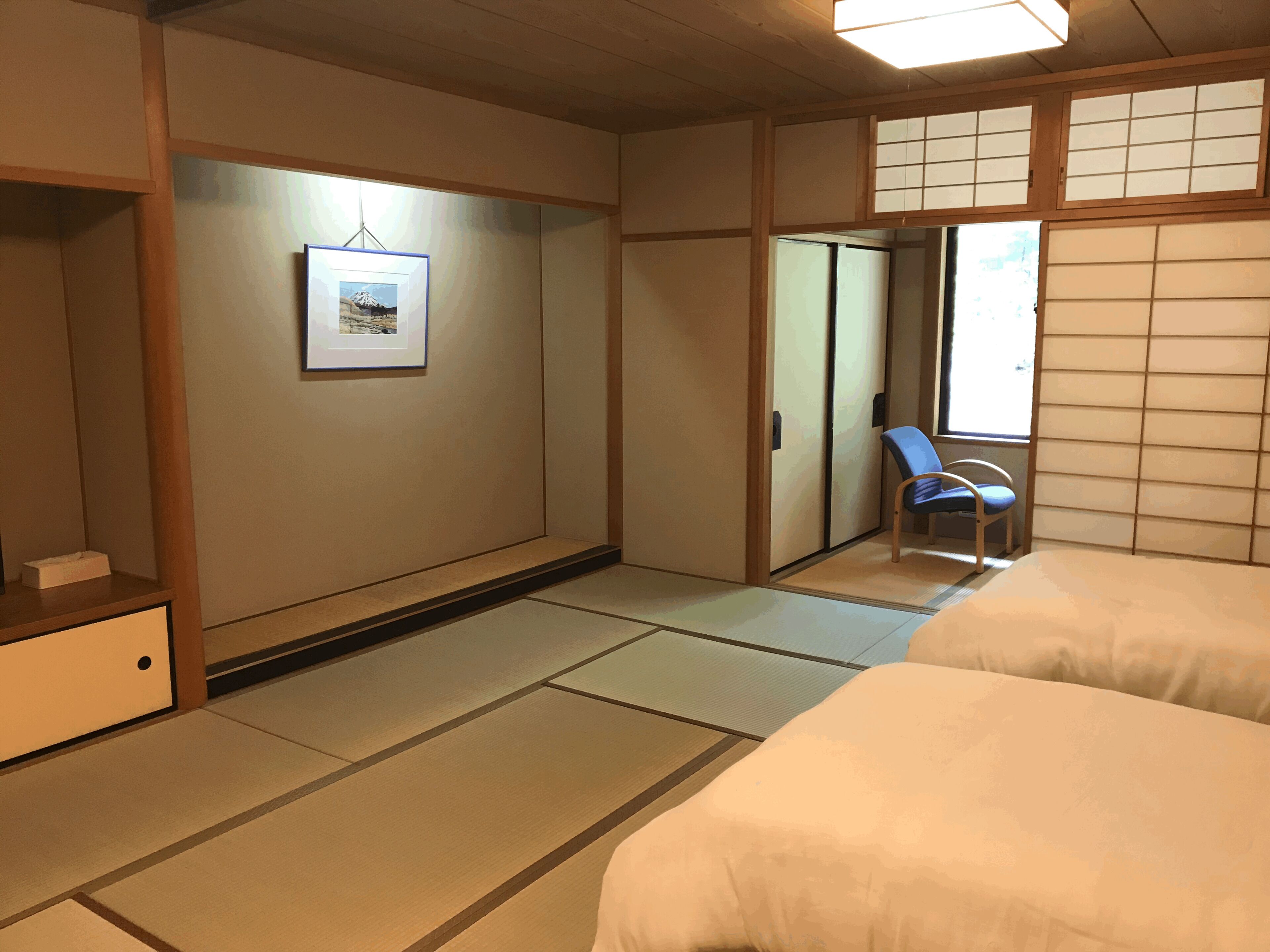 A traditional Japanese room with tatami flooring, a bed, a chair, and a sliding door.