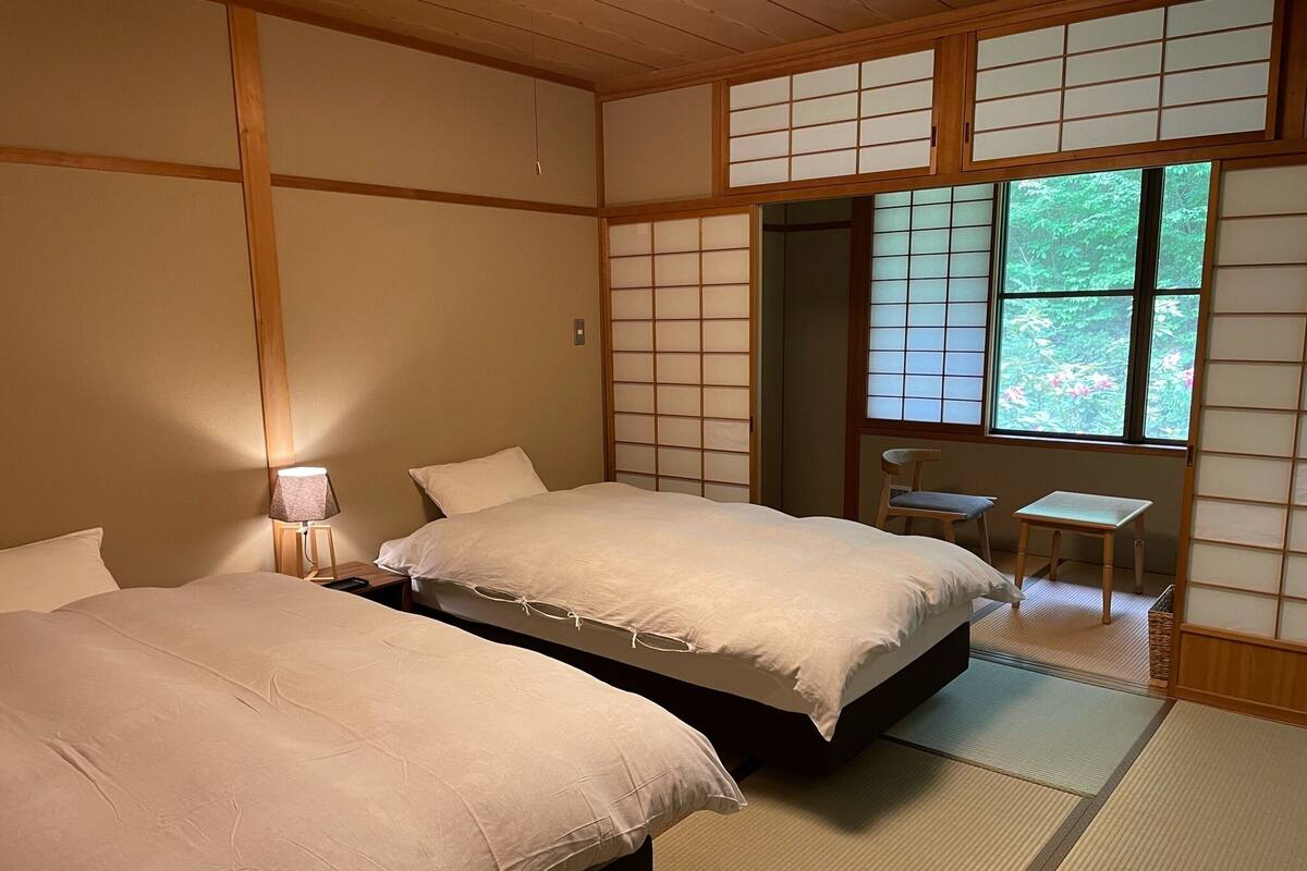 Ein traditioneller japanischer Raum mit Tatami-Böden, zwei Betten, einem kleinen Tisch und einer Schiebetür zum Garten.