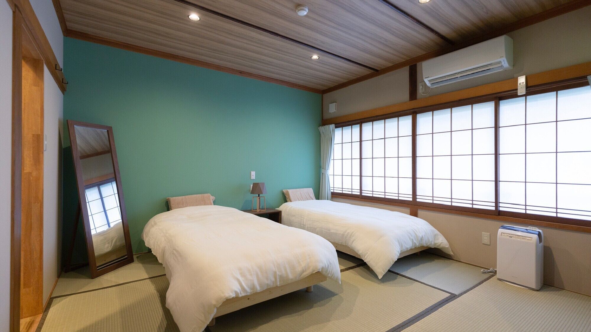 A room with two beds, a mirror, a lamp, and a window with a view.