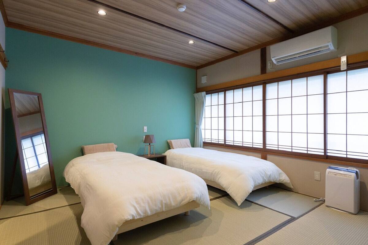 Ein Zimmer mit zwei Betten, einem Spiegel, einer Lampe und einem Fenster mit Blick.