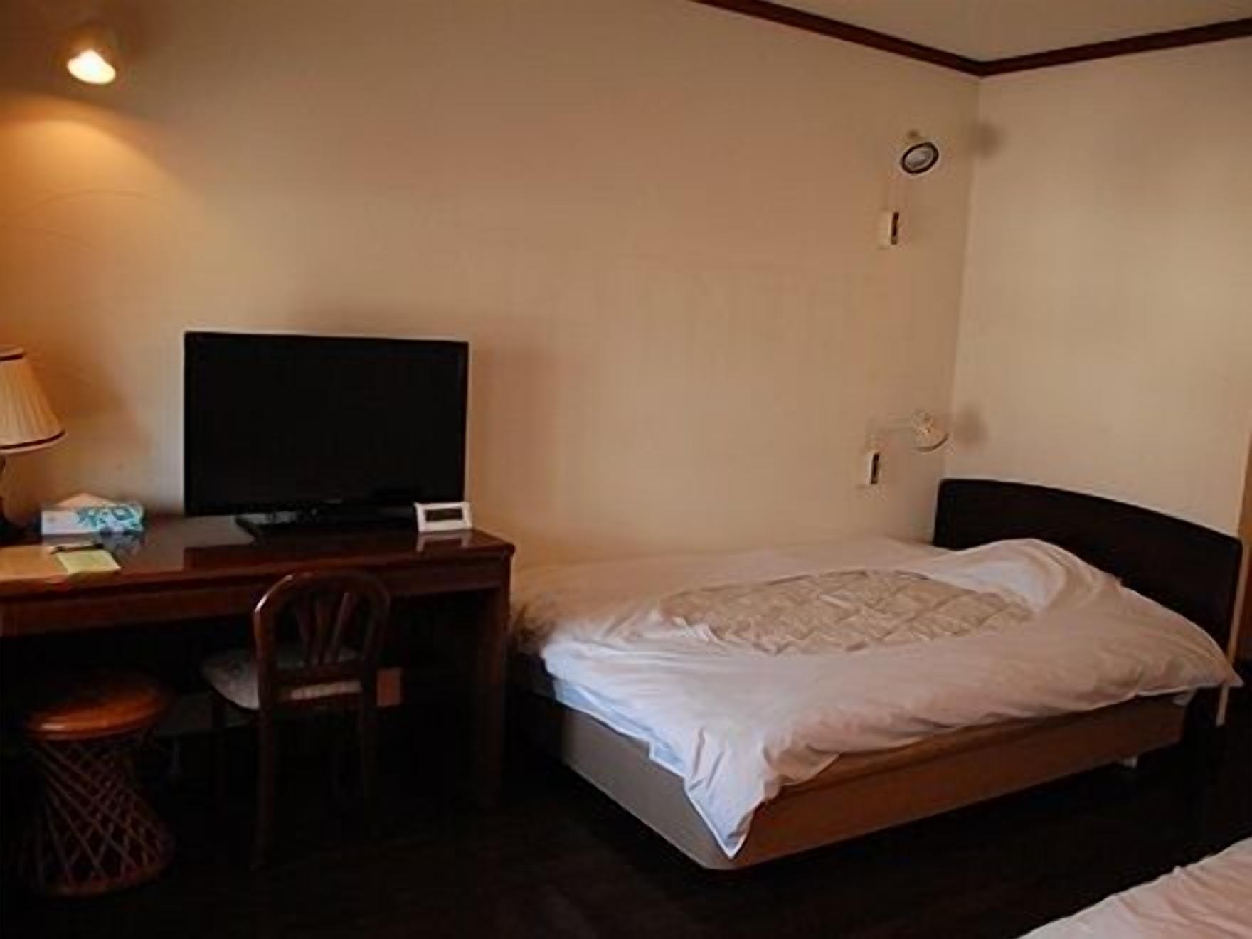 Ein Hotelzimmer mit einem Bett, einem Schreibtisch mit Fernseher, einem Sessel und einem Mülleimer.
