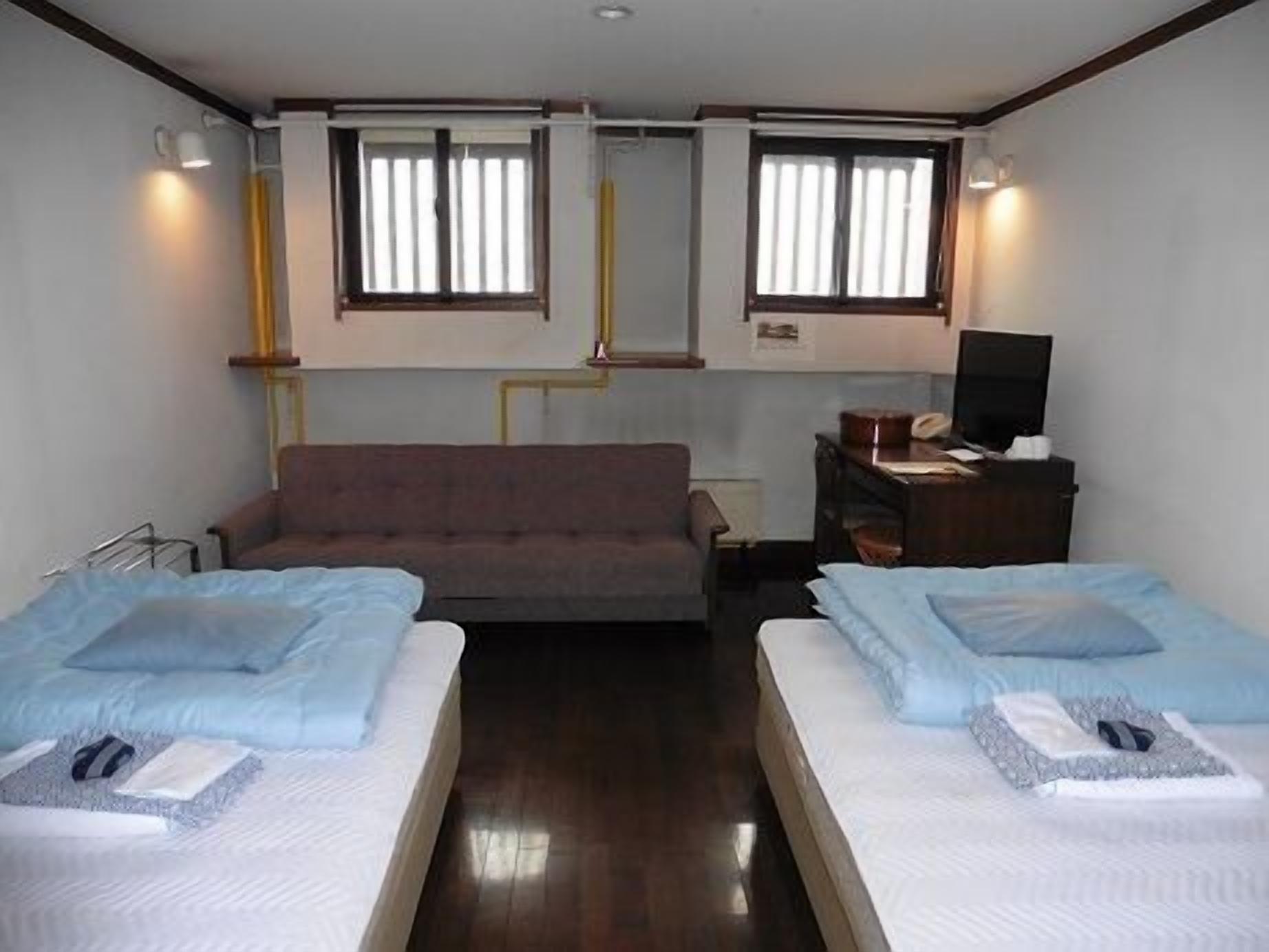 Ein Zimmer mit zwei Betten, einem Sofa, einem Schreibtisch mit Stuhl und zwei Fenstern mit Vorhängen.