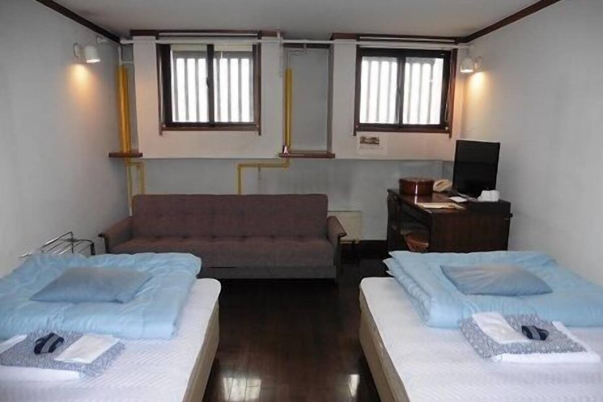 Une chambre avec deux lits, un canapé, un bureau avec une chaise et deux fenêtres avec des rideaux.