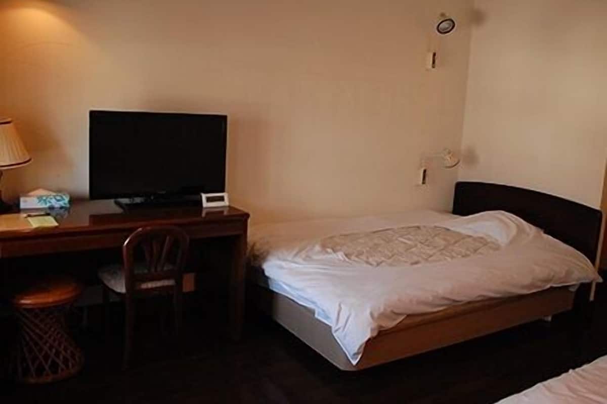 Ein Hotelzimmer mit Bett, Schreibtisch, Fernseher, Stuhl und Mülleimer.