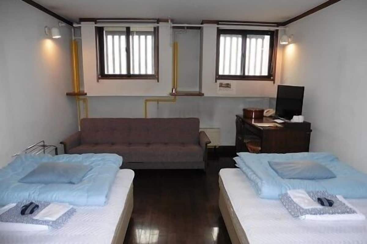 Une chambre d’hôtel avec deux lits, un canapé, un bureau avec une chaise et deux fenêtres avec des rideaux.